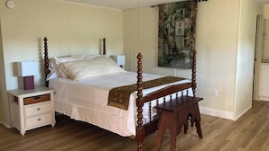 Een slaapkamer met een hemelbed, een nachtkastje met lades, een bijzettafeltje en een plafondventilator.