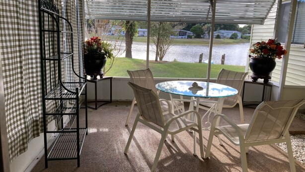 Een overdekt terras met een tafel, stoelen, een metalen rek en uitzicht op een meer.