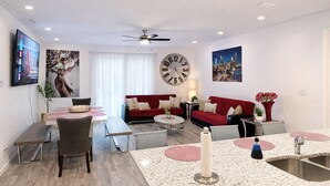 A modern living room with a dining area, red sofas, a large wall clock, and a ceiling fan.