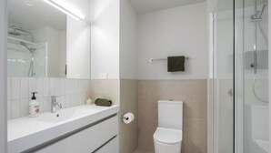A modern bathroom with a large mirror, a sink, a toilet, and a shower area. - Waihi Beach Retreat (#B7) (Waihi Beach)