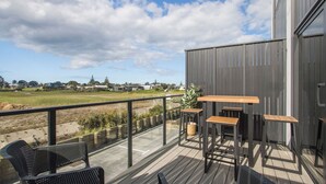 A deck with outdoor furniture, a view of a field, and a building in the background. - Waihi Beach Retreat (#B7) (Waihi Beach)