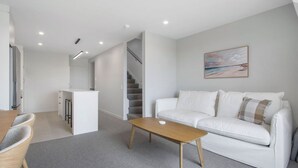 A modern living room with a white sofa, a wooden coffee table, and a painting on the wall. - Waihi Beach Retreat (#B7) (Waihi Beach)