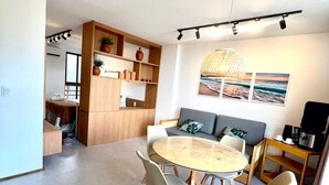 A modern living room with a round dining table, two sofas, a coffee machine, and a large window. - Seaside Studio II at “ecologic route of Milagres (Porto de Pedras)