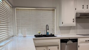 Una cocina con armarios blancos, un lavamanos de acero inoxidable y un lavavajillas.