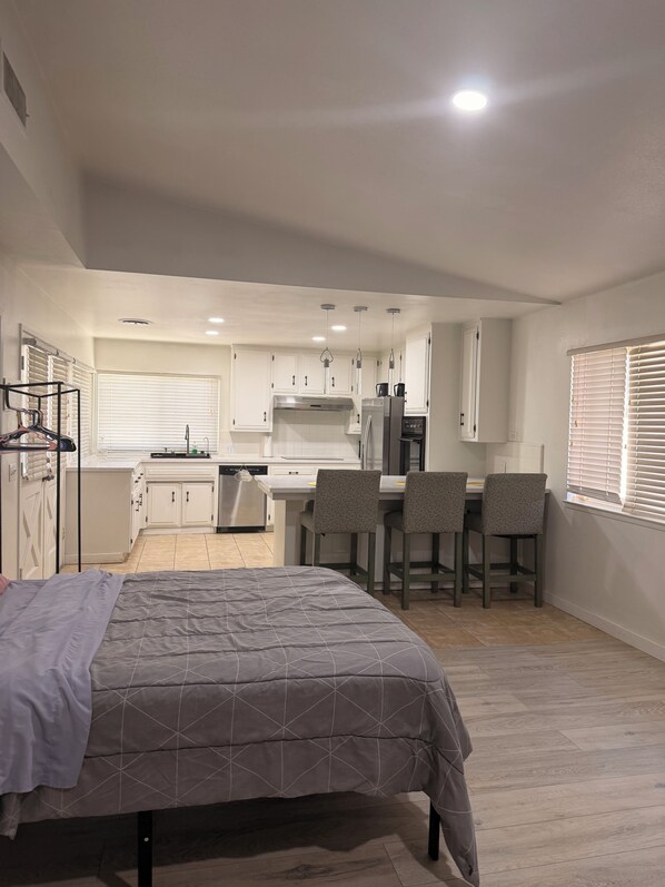 A compact room with a bed, a kitchenette, and a dining area with chairs.