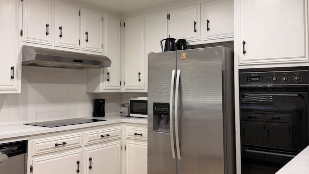 Una cocina con armarios blancos, electrodomésticos de acero inoxidable y suelo de baldosas.