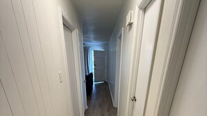 A hallway with white walls, wooden flooring, and doors leading to other rooms. - Newly Renovated 3 Bedroom House in Lakewood (Durham)