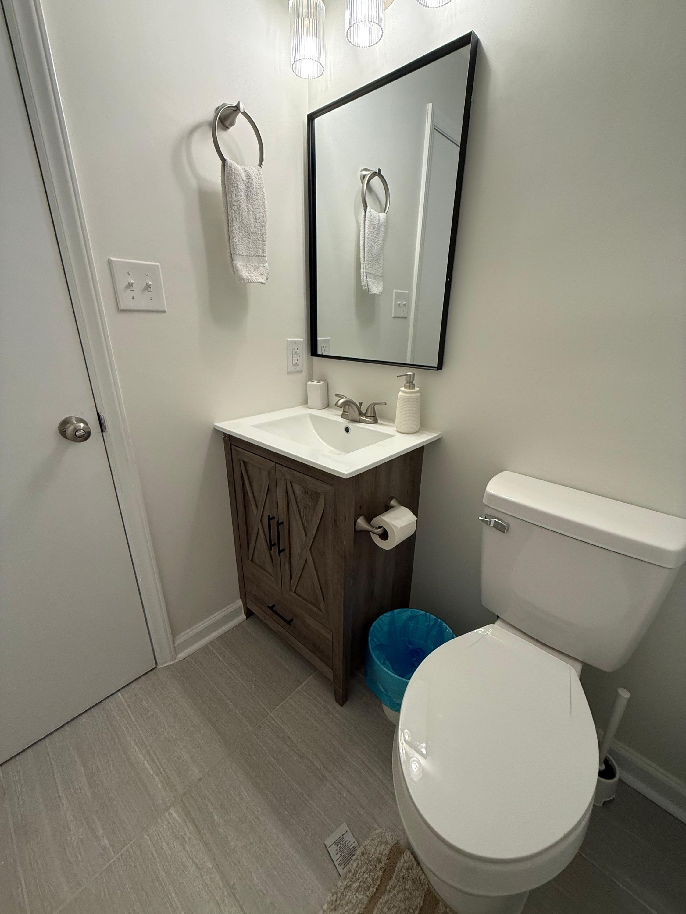 A bathroom with a white toilet, a wooden vanity with a sink, and a mirror above the mirror.