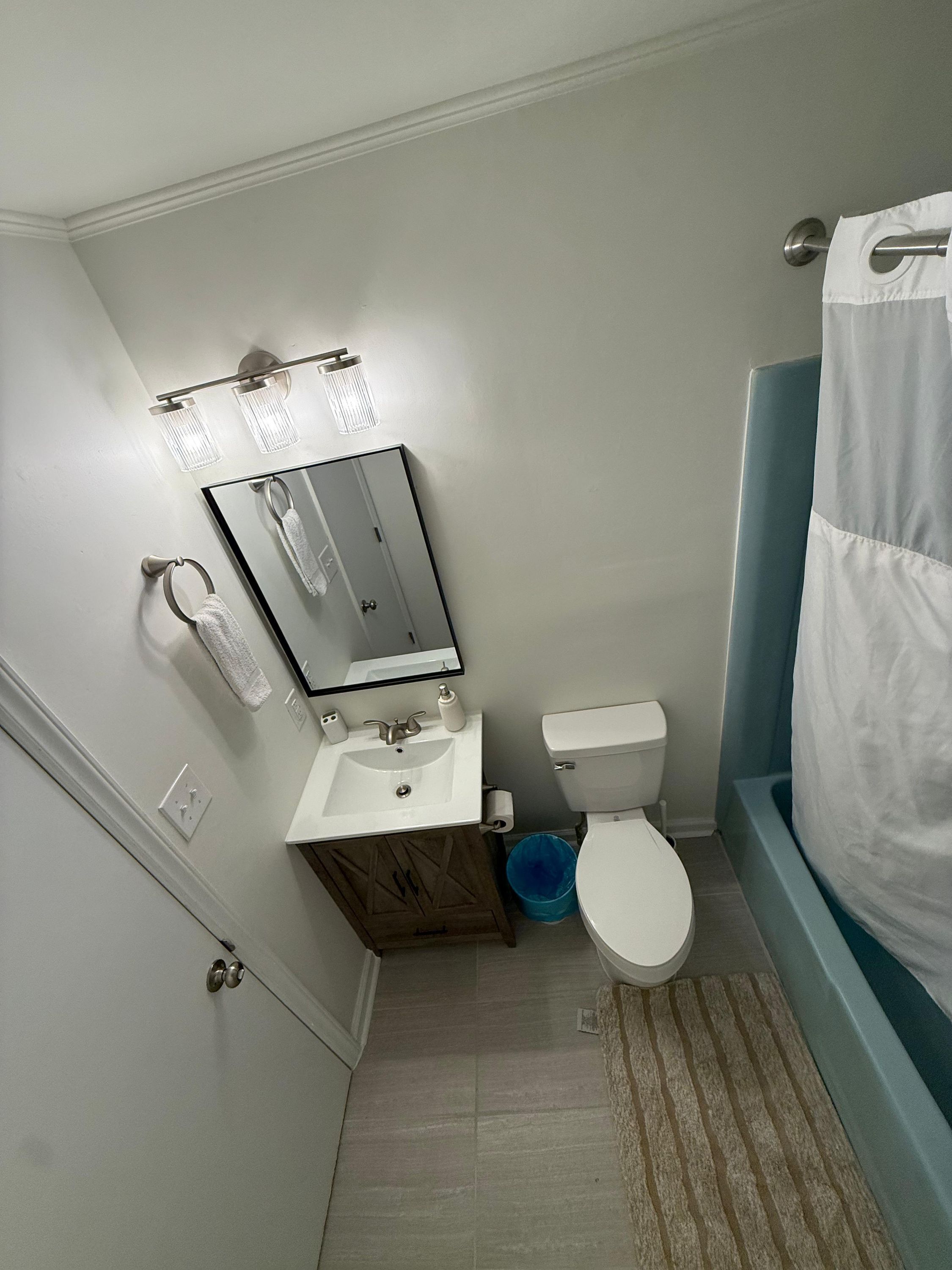 Ein kleines Badezimmer mit einem weißen Waschbecken, Spiegel, WC und einer blauen Duschvorhang.