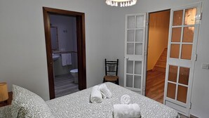 A bedroom with a bed, a hanging light fixture, a chair, and a door leading to a bathroom. - Villa Bellavista (Olvera)