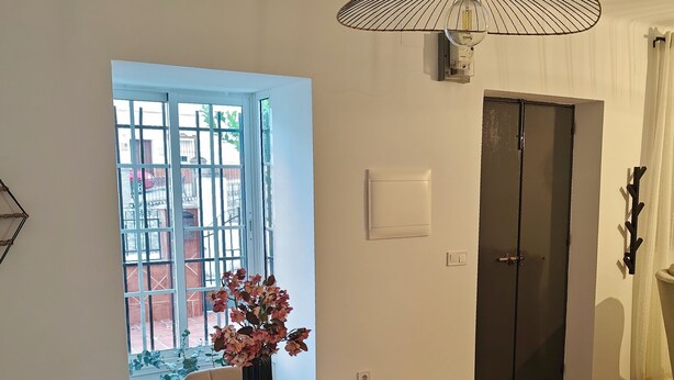 A modern dining area with a wooden table, chairs, a vase with flowers, a pendant light, and a view through a window. - Villa Bellavista (Olvera)