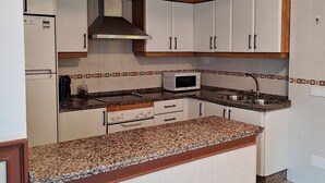 A compact kitchen with white cabinets, a granite countertop, a microwave, and a stainless steel sink. - Villa Bellavista (Olvera)
