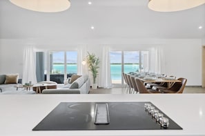 Una habitación de hotel moderna con comedor, ventanas amplias con vista al océano y una mesa central con sillas.