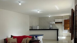A modern living room with a red sofa, a brown ottoman, a small round table, and a kitchen area in the background.