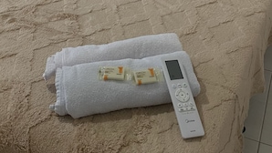 Een bed met een beige deken, twee beige kussens, een witte afstandsbediening en twee Grion verpakkingen op een witte handdoek.