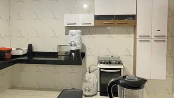 Uma cozinha com armários brancos, fogão, chaleira e cafeteira.