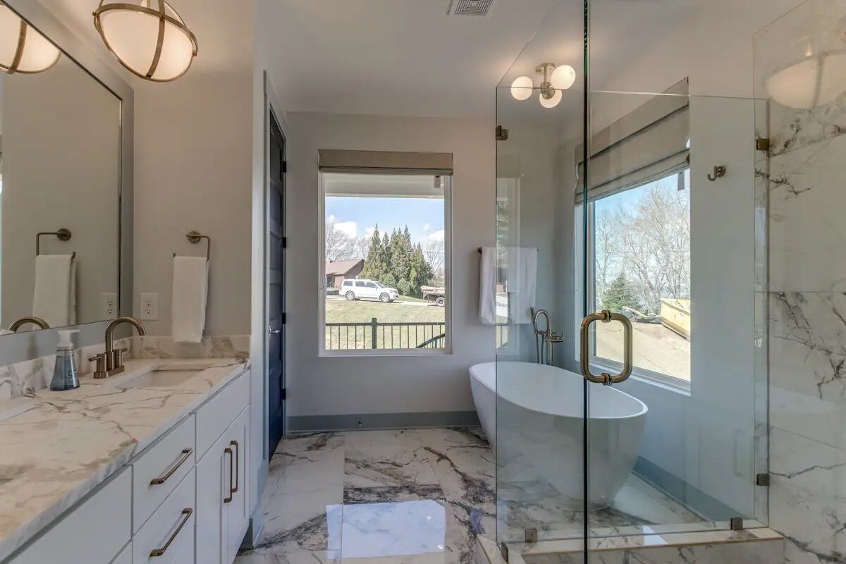 A modern bathroom with a glass-enclosed shower, a large mirror, and a view of the outside.