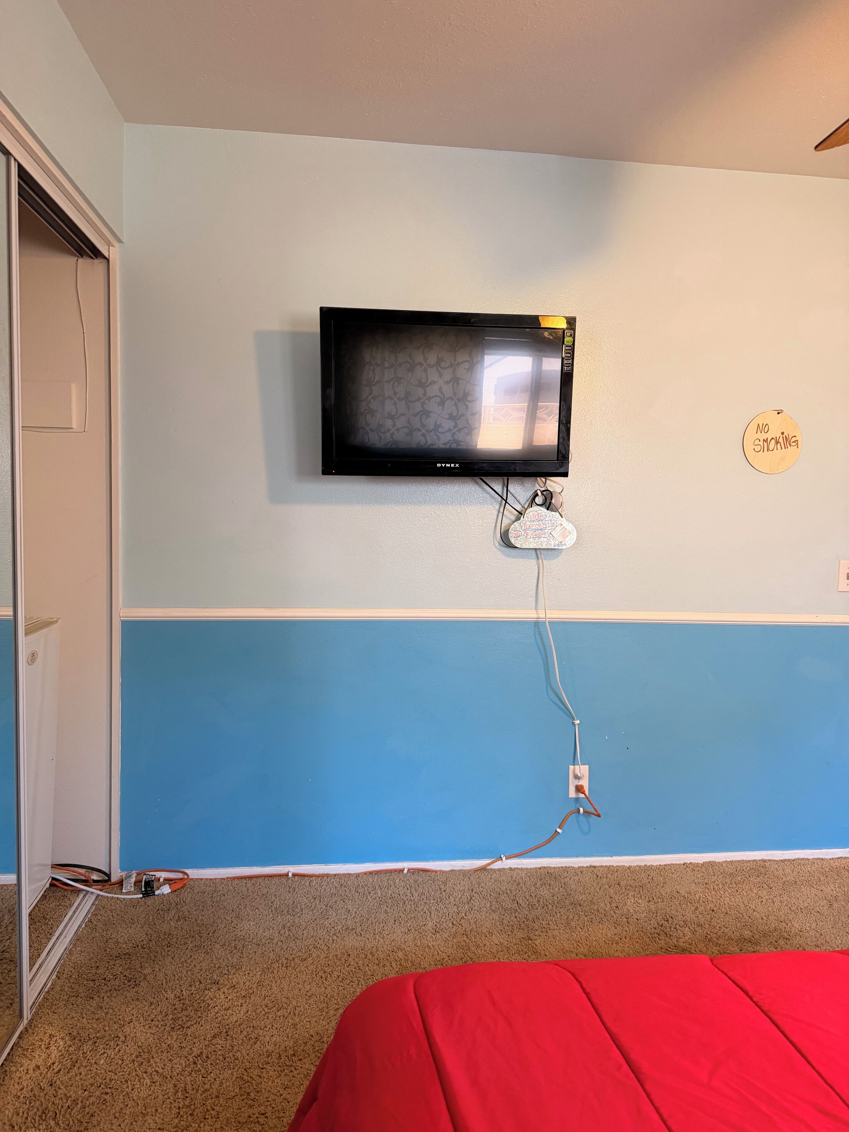 Une chambre avec un téléviseur fixé au mur, un panneau indiquant « il est interdit de fumer » et un lit rouge.