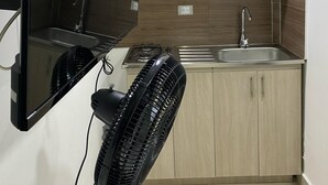 A kitchen with wooden cabinets, a sink, a stove, and a black fan. - Hotel Ciento Once Boutique (Medellín)
