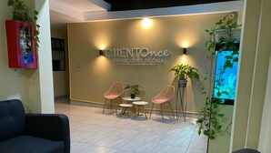 A modern interior with a reception desk, two chairs, a small table, and a potted plant. - Hotel Ciento Once Boutique (Medellín)