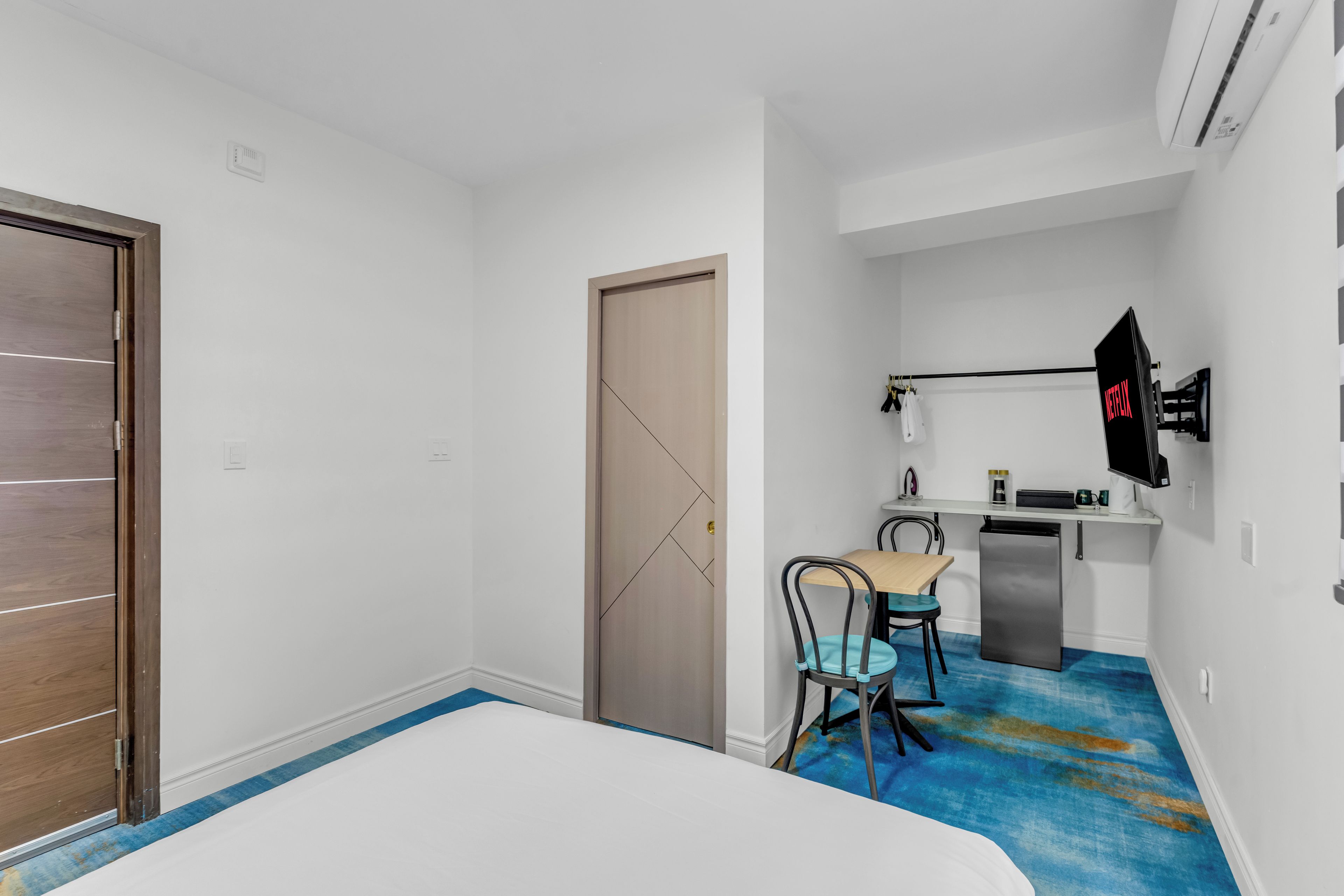 Une chambre d’hôtel comprenant un lit, un bureau avec une chaise, une petite kitchenette et un téléviseur fixé au mur.