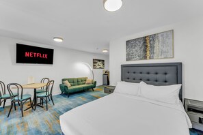 A hotel room with a bed, a desk with a chair, a sofa, a television displaying 'NETFLIX', and a painting on the wall. - Plush Hotel (toronto)