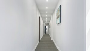 A long, narrow hallway with white walls, a gray carpet, and recessed ceiling lights. - Plush Hotel (toronto)