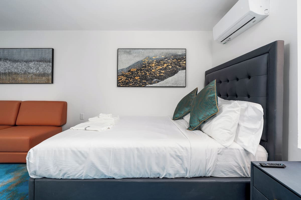 Moderni hotellihuone, jossa on sänky, sohva ja kaksi seinälle asennettua taideteosta.