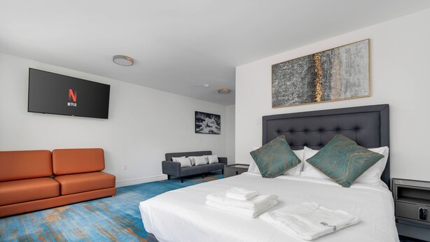 A hotel room with a bed, a TV mounted on the wall, a sofa, and a painting. - Plush Hotel (toronto)