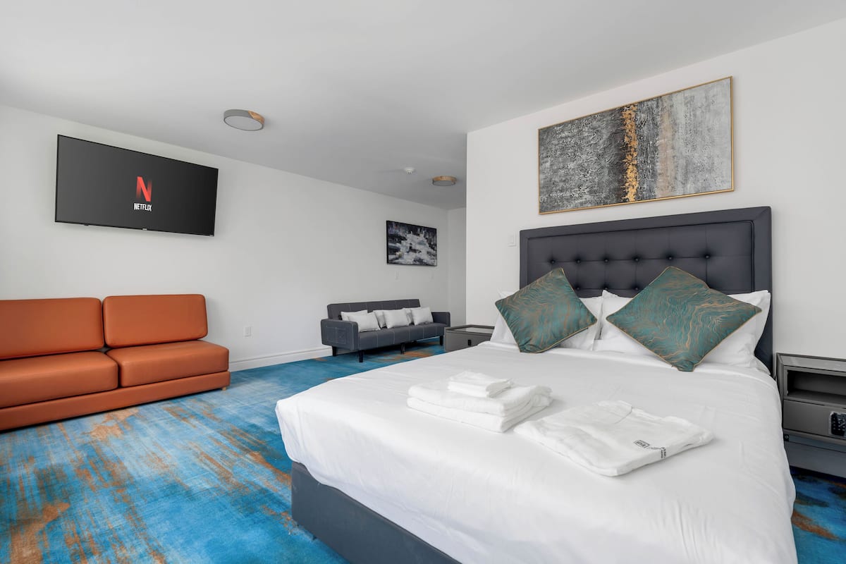 Hotellihuone, jossa on sänky, seinälle asennettu televisio, sohva ja taulu.