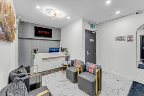 Un vestíbulo de hotel moderno con mostrador de recepción, zona de estar y un televisor que muestra 'NETFLIX'.