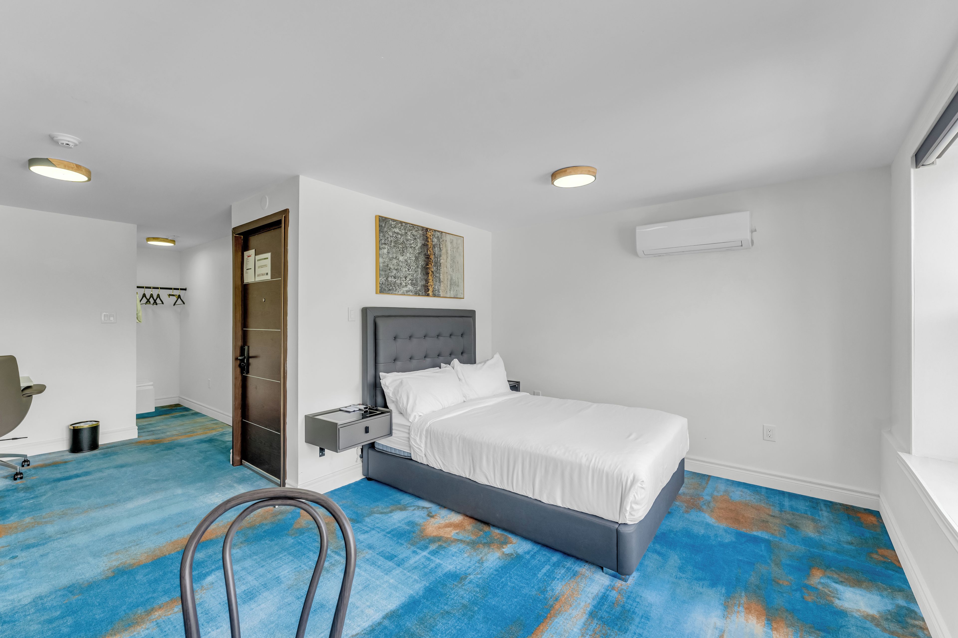 Un dormitorio moderno con cama, mesitas de noche, una silla y una puerta.
