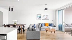 A modern living room with a grey sofa, a wooden coffee table, and a dining area with a white table and chairs. - chevron /3beds / Pool /Parking n Ocean glimpses (Surfers Paradise)