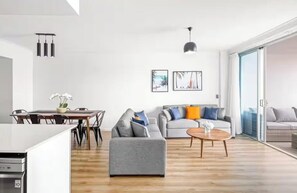 A modern living room with a grey sofa, a wooden coffee table, and a dining area with a white table and chairs. - chevron /3beds / Pool /Parking n Ocean glimpses (Surfers Paradise)