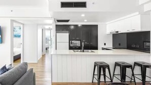 A modern kitchen with white cabinetry, a central island, and black bar stools. - chevron /3beds / Pool /Parking n Ocean glimpses (Surfers Paradise)