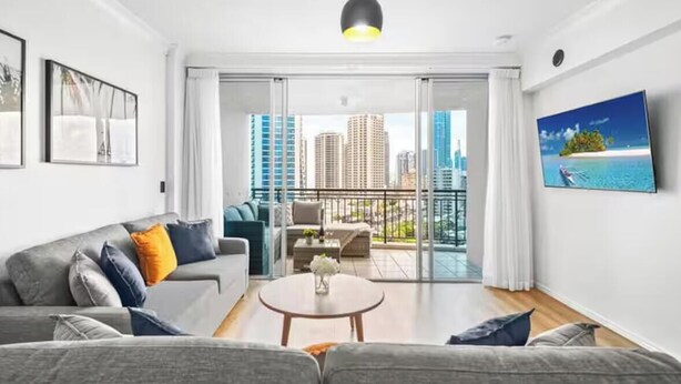 A modern living room with a grey sofa, a round coffee table, and a TV on the wall. - chevron /3beds / Pool /Parking n Ocean glimpses (Surfers Paradise)