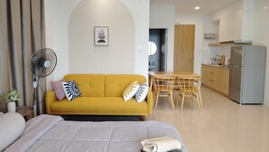 Una habitación de hotel moderna con cama, sofá amarillo, mesa de comedor y kitchenette.