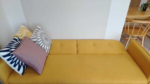 Un sofá amarillo con cojines estampados en una habitación con una mesa y sillas de madera.