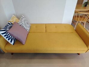 A yellow sofa with patterned cushions in a room with a wooden table and chairs. - Kuching Suite Ace @ Riverine Diamond (Kuching)