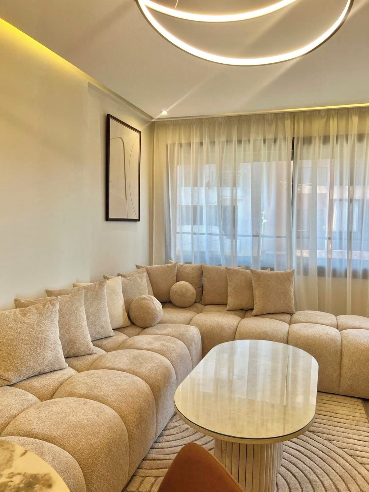 A modern living room with a sectional sofa, a glass coffee table, and sheer curtains.