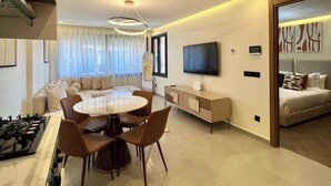 A modern living room with a dining area, a flat-screen TV mounted on the wall, and a sofa set. - Cocon Plaza (Marrakech)