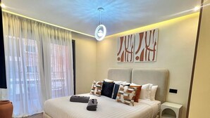 A modern bedroom with a large bed, a bedside table, a floor lamp, and abstract wall art. - Cocon Plaza (Marrakech)