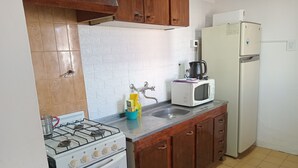 Una cocina equipada con estufa a gas, horno, microondas, refrigerador y pileta.