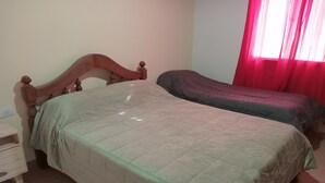 Un dormitorio con dos camas, una mesita de noche y una ventana con cortinas rojas.