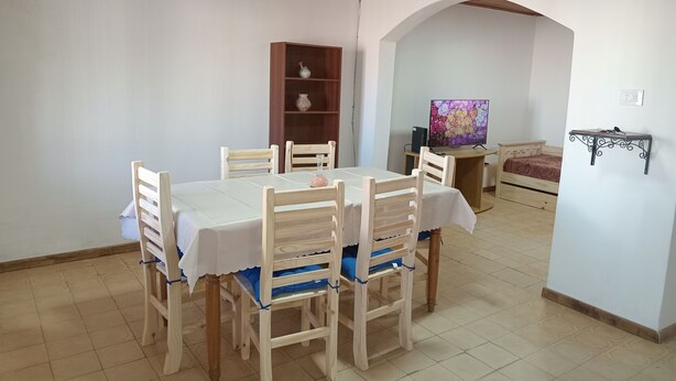 Un comedor con una mesa y sillas, una estantería, un televisor y una cama.