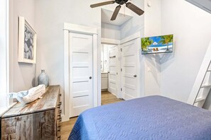 A bedroom with a bed, a ceiling fan, a TV, a framed picture, and a door leading to a bathroom. - BQ1B - Cozy Corolla Retreat Near Beach & Community Pool (Corolla)