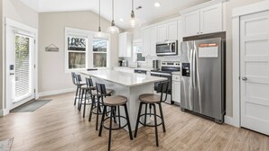 A modern kitchen with a large island, stainless steel appliances, and bar stools. - BQ1B - Cozy Corolla Retreat Near Beach & Community Pool (Corolla)