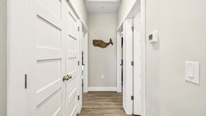 A hallway with white doors, a wooden floor, and a wall-mounted light switch. - BQ1B - Cozy Corolla Retreat Near Beach & Community Pool (Corolla)