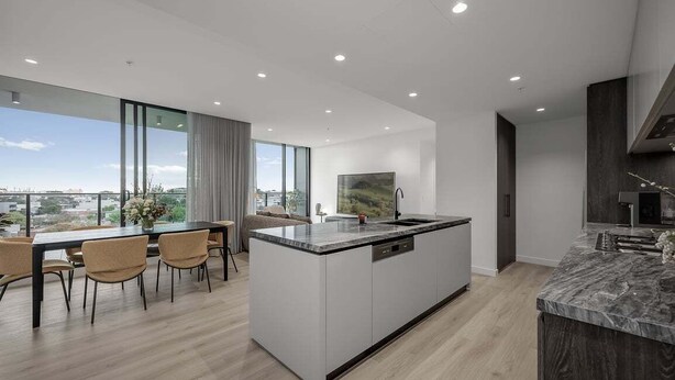 A modern kitchen with a large island, dining area with chairs, and a view through large windows. - Ocean Glimpse - A 3-Bedroom Designer Sub-Penthouse @ 333STK (Port Phillip)