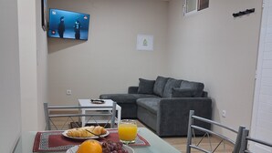 A dining table with breakfast items, a grey sofa, and a TV in a living area. - Arco-Íris, Ponta do Sol (Ponta do Sol)